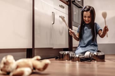 girl playing with pots and pans on floor with teddy bear in foreground